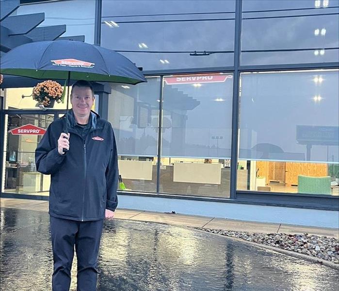 male SERVPRO employee standing outside building with umbrella