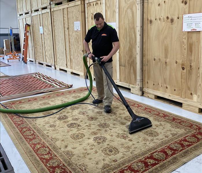 male SERVPRO employee cleaning area rug in warehouse