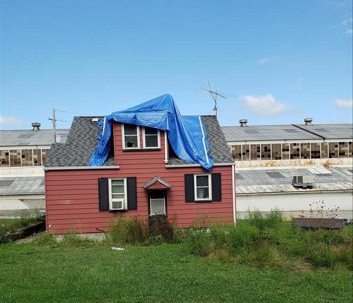 A blue tarp is covering damage on a roof.