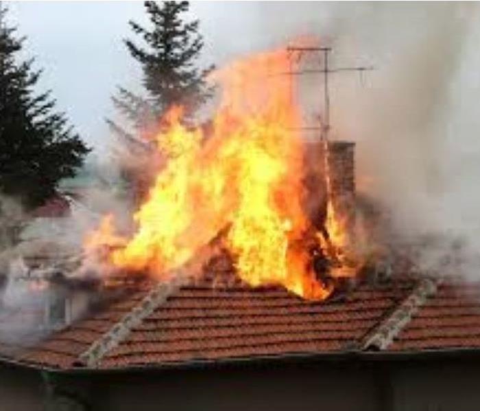 roof of house engulfed in flames with smoke coming from the sides 
