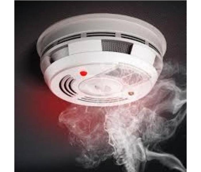 white smoke detector with red light lit and smoke coming from the bottom