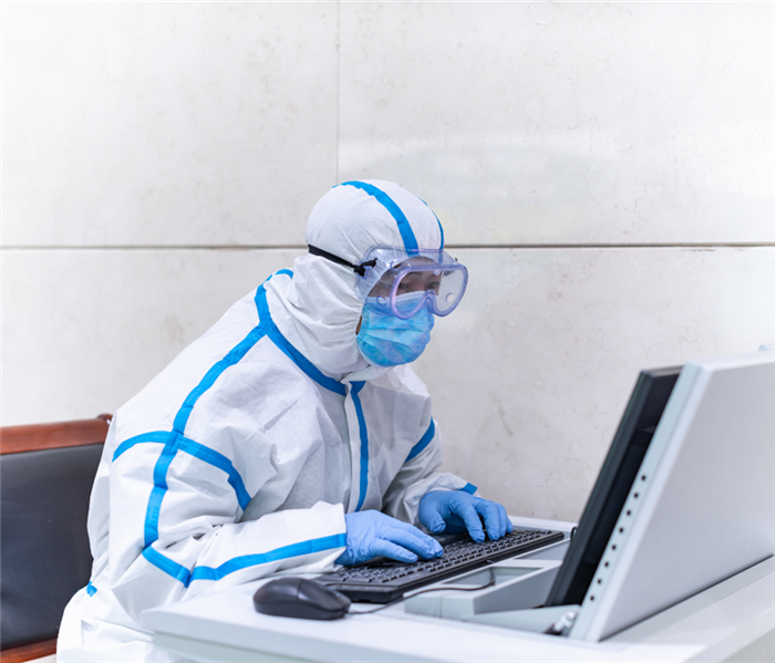 picture shows a person working from a computer covered in PPE