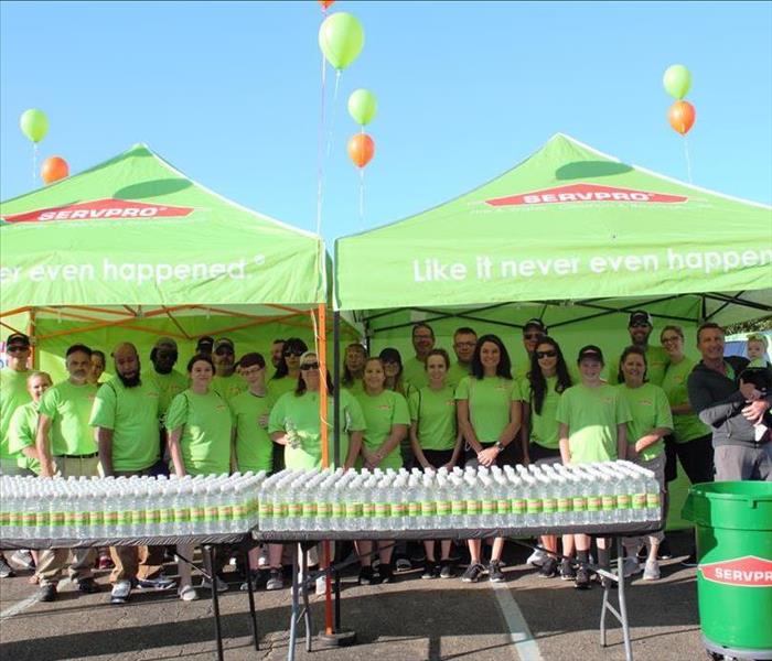 members of SERVPRO in SERVPRO green t-shirts, rows of water bottles sit on two tables under two green SERVPRO tents