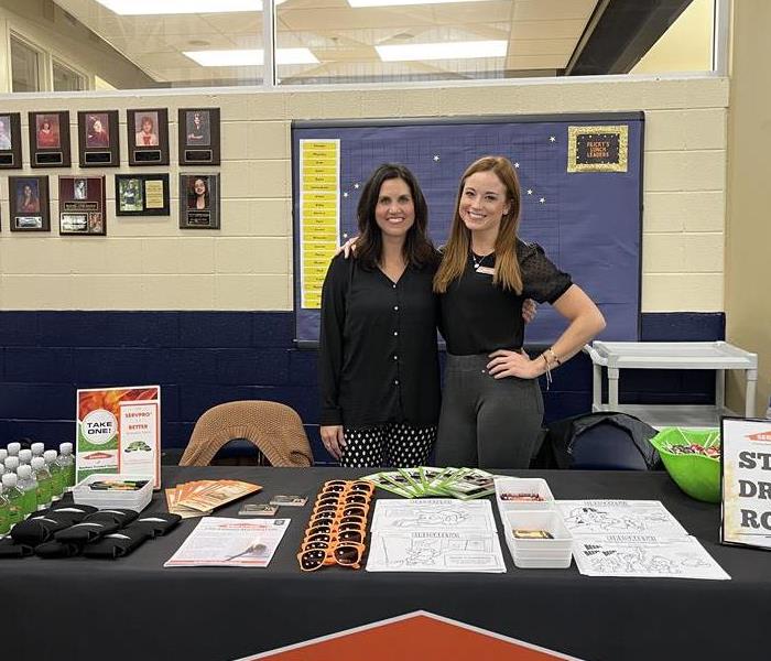 Two female SERVPRO employees standing behind promotional table at event